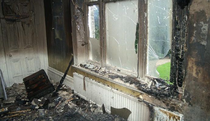 Interior of a fire-damaged room with shattered windows, charred walls and debris scattered on the floor